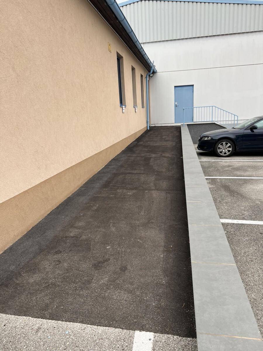 Außenansicht eines Gebäudes mit einer asphaltierten Rampe und einem angrenzenden Parkplatz.