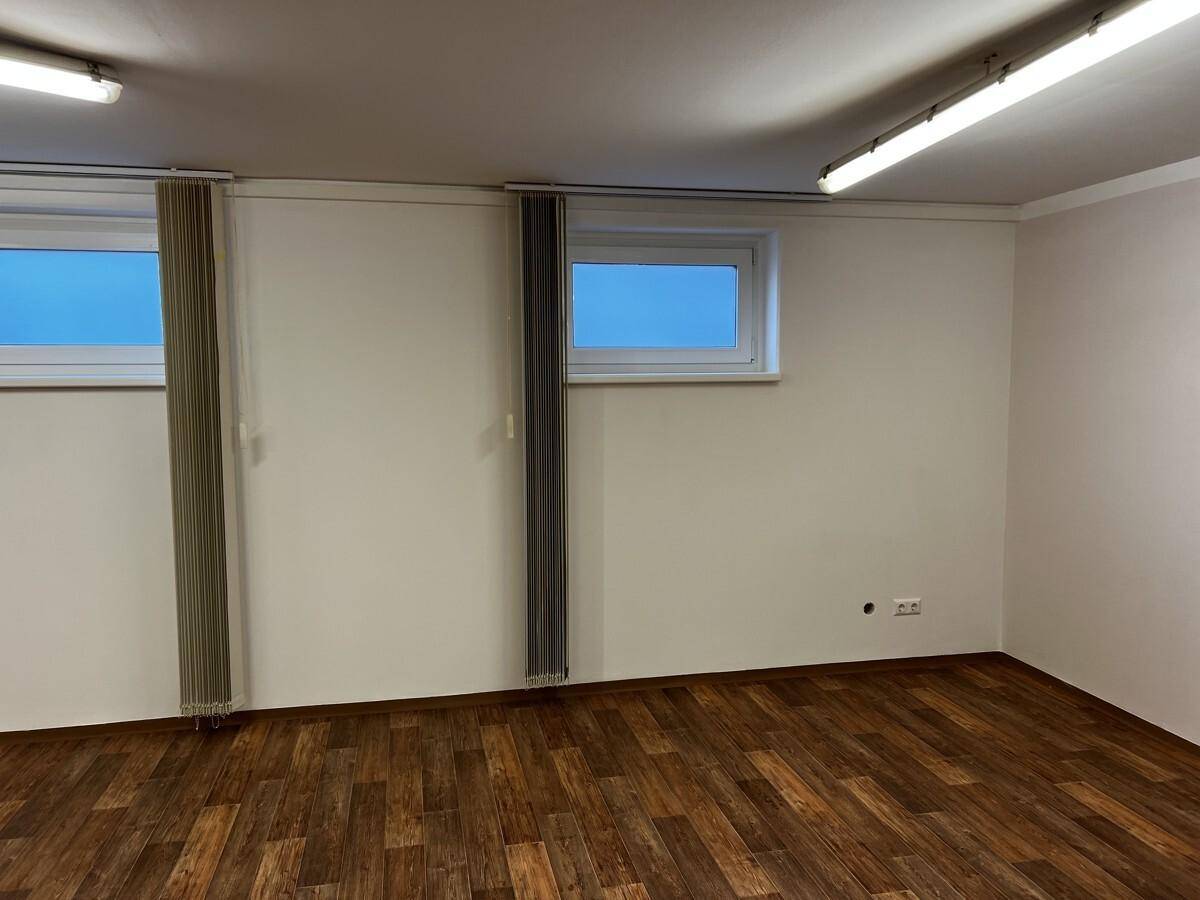 Nahaufnahme der weißen Wand mit zwei kleinen Fenstern, vertikalen Jalousien und einem Heizkörper.