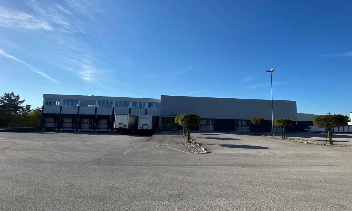 Gewerbegebäude mit mehreren Laderampen und großem Parkplatz unter blauem Himmel.