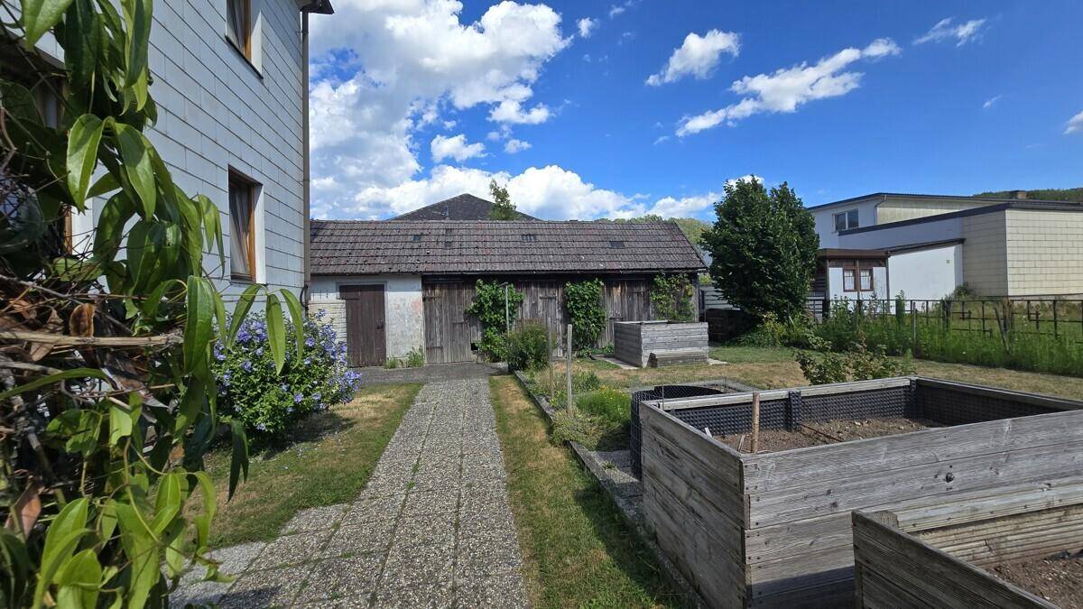 Blick auf den Garten mit Hochbeeten, einem alten Schuppen und dem Haus im Hintergrund.