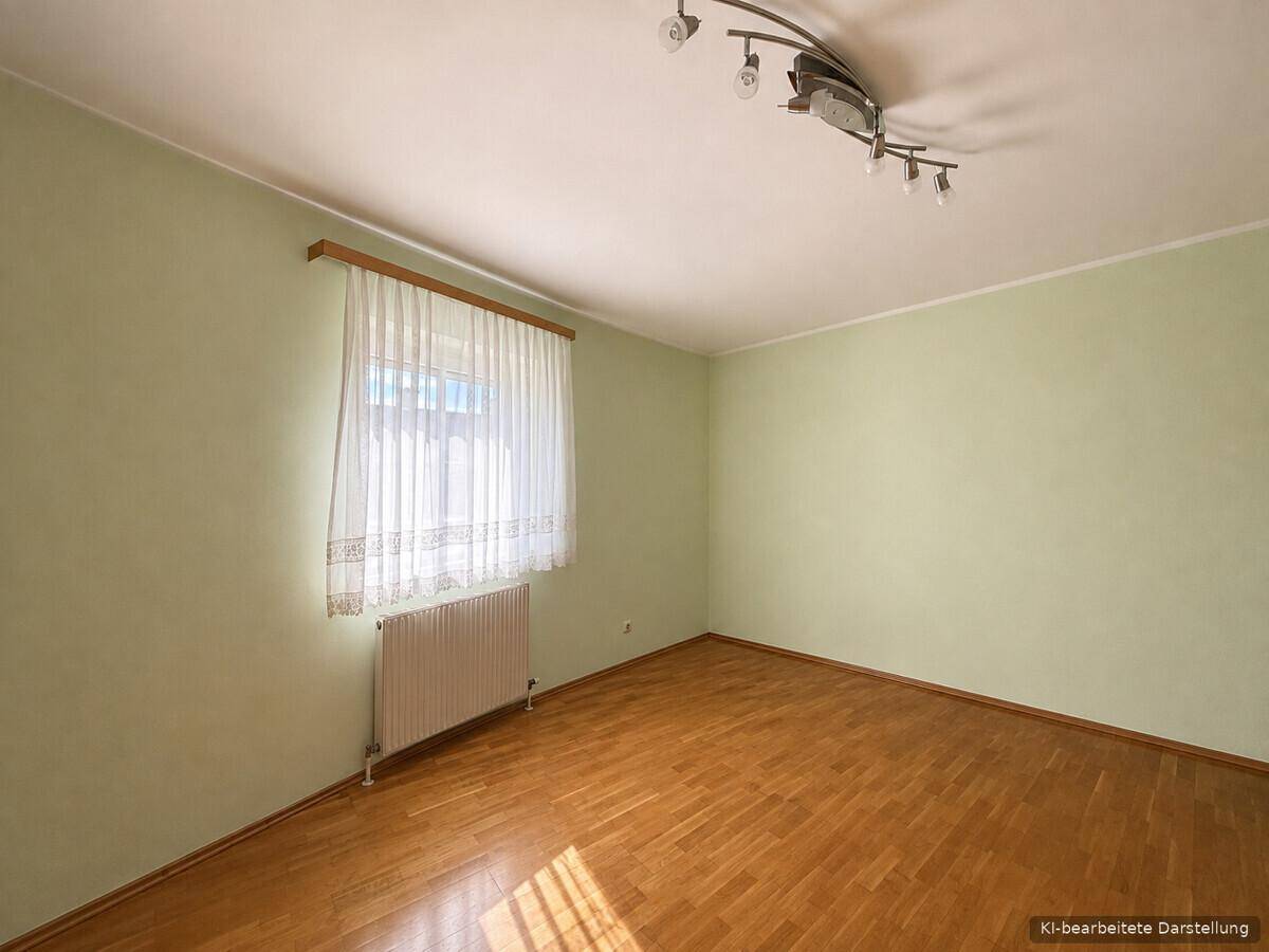 Freundliches Zimmer mit Parkettboden, grünen Wänden und einem Fenster mit hellem Vorhang.