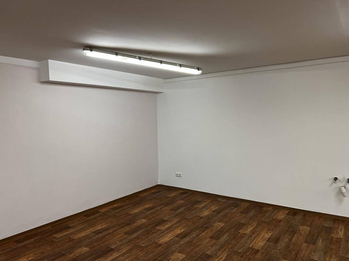 Ecke des Raumes mit weißen Wänden, dunklem Laminatboden und sichtbaren Anschlüssen für mögliche Installationen.