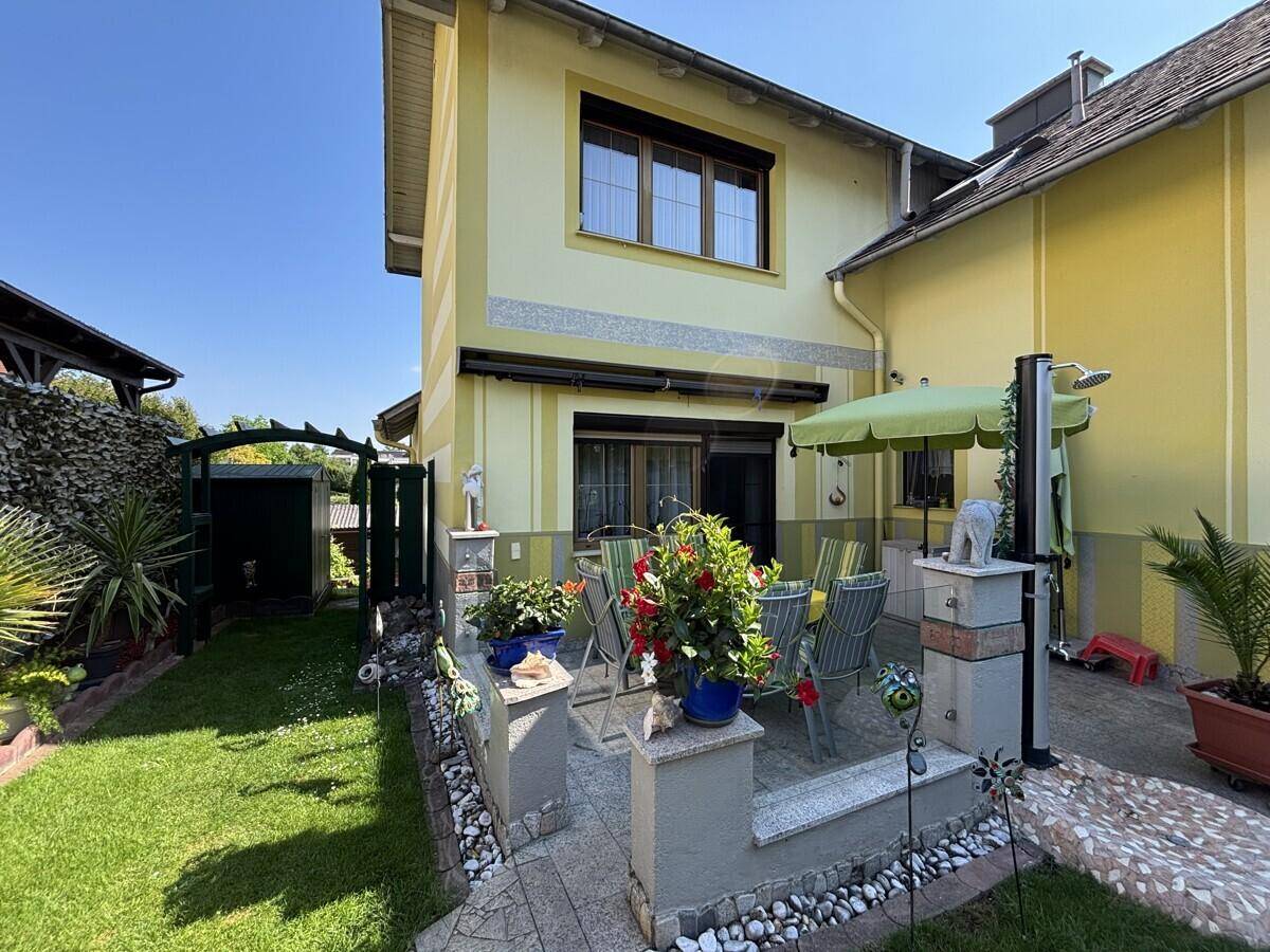 Gemütliche Terrasse mit Gartenmöbeln und angrenzendem Rasenbereich an einem sonnigen Tag.