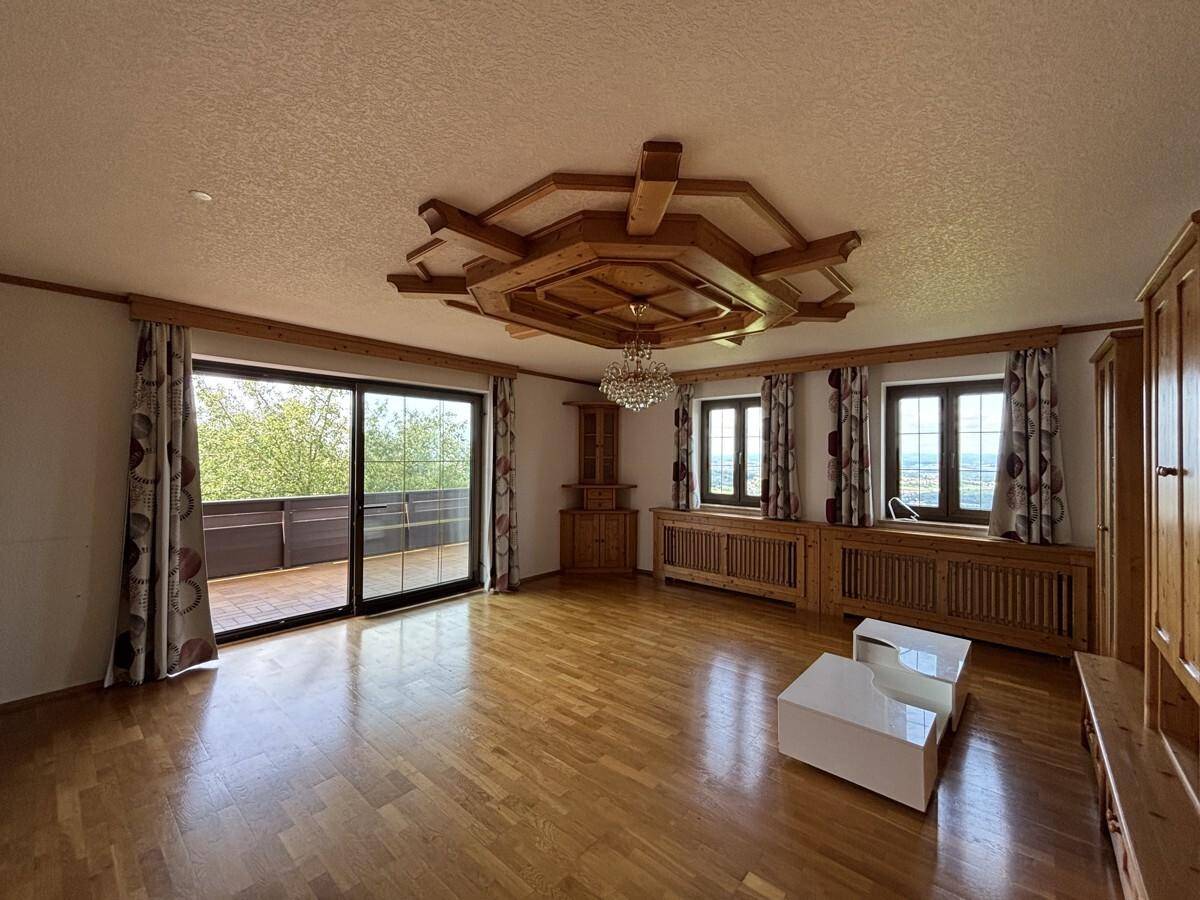 Helles Wohnzimmer mit Holzparkett, dekorativer Holzdecke und Zugang zu einem Balkon mit Weitblick.