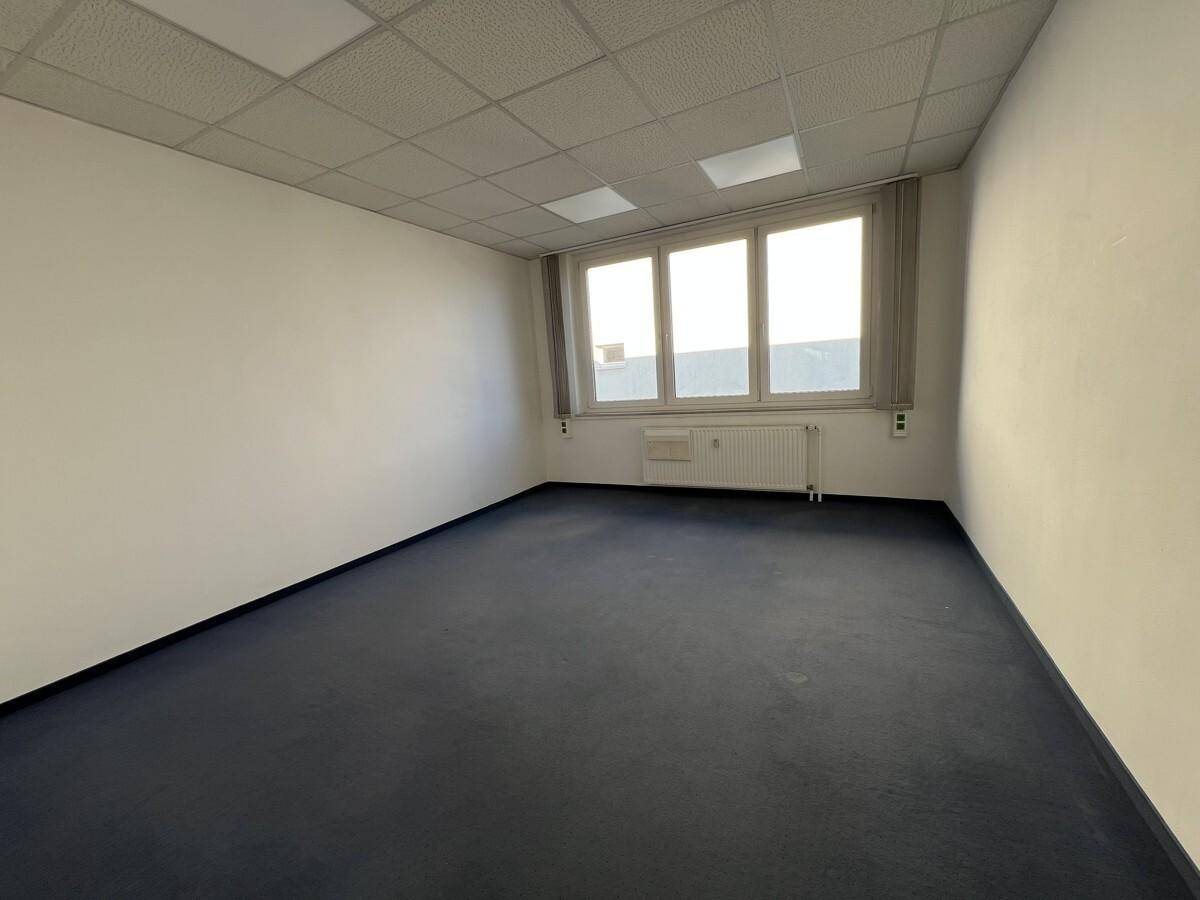 Leeres Büro mit viel Tageslicht durch große Fenster und einem blauen Teppichboden.