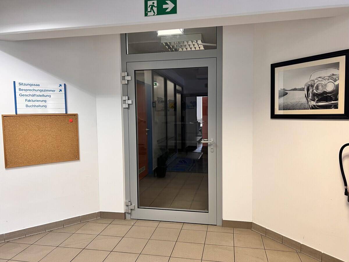 Innenflur mit einer Glastür, die zu weiteren Büroräumen führt, und einem schwarzen gerahmten Bild.