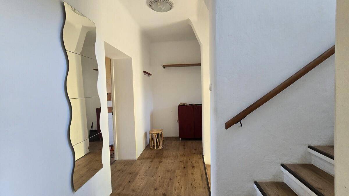 Heller Flur mit Holzfußboden, einem großen Spiegel und Zugang zur Treppe.