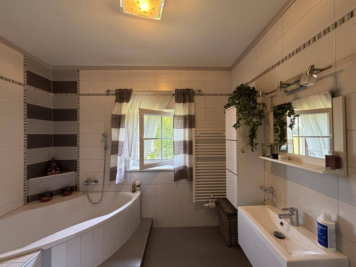 Helles Badezimmer mit Badewanne, modernem Waschtisch und Fenster für natürliche Belüftung.