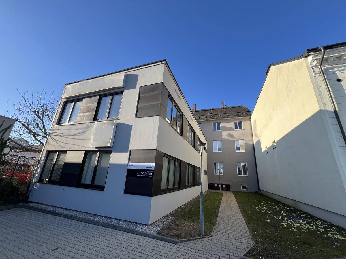 Ansicht eines modernen Bürogebäudes mit klaren Linien und angrenzenden älteren Gebäuden.
