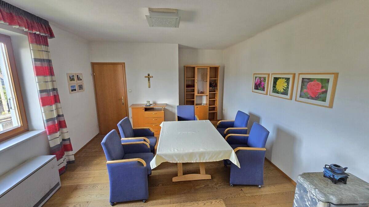 Geräumiges Esszimmer mit Holzboden, großem Tisch, blauen Stühlen und schlichter Dekoration.