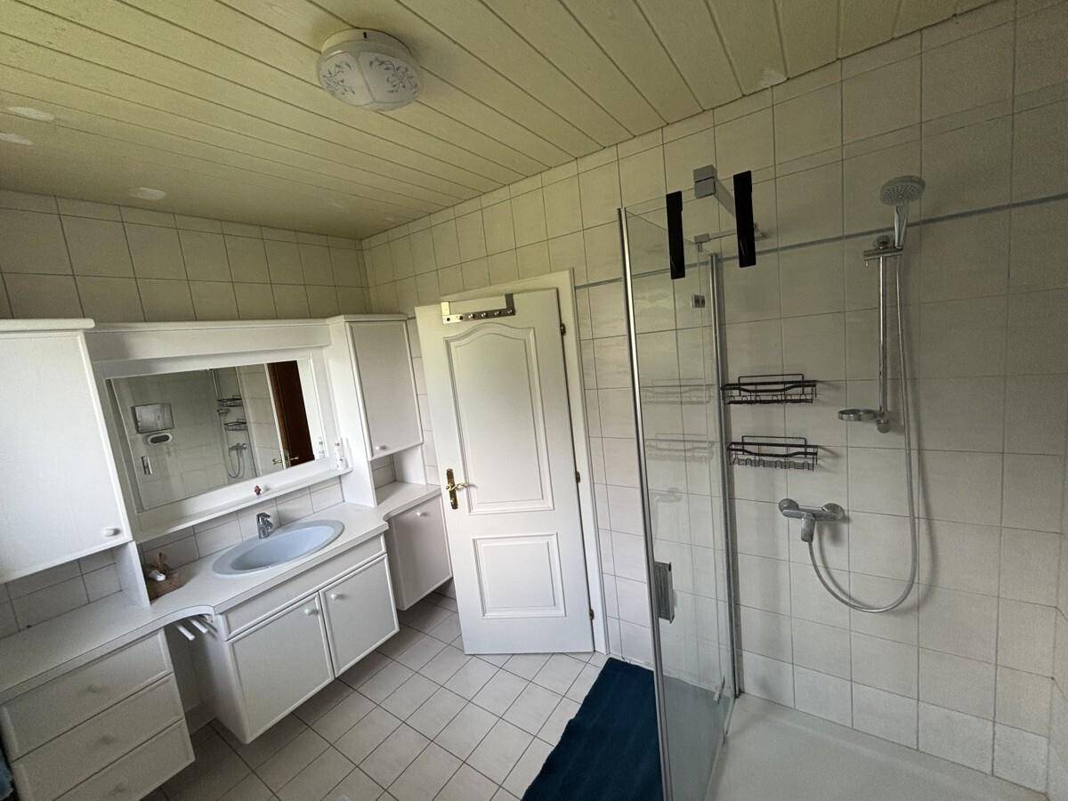 Helles Badezimmer mit weißen Fliesen, Einzelwaschbecken und moderner Glasduschkabine.