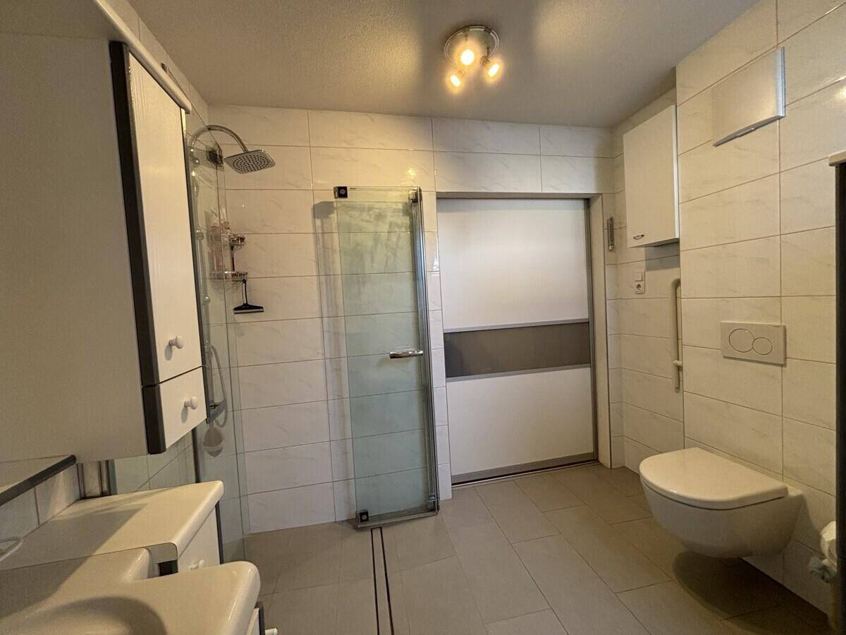 Helles Badezimmer mit Duschkabine, wandmontierter Toilette und modernen Fliesen.