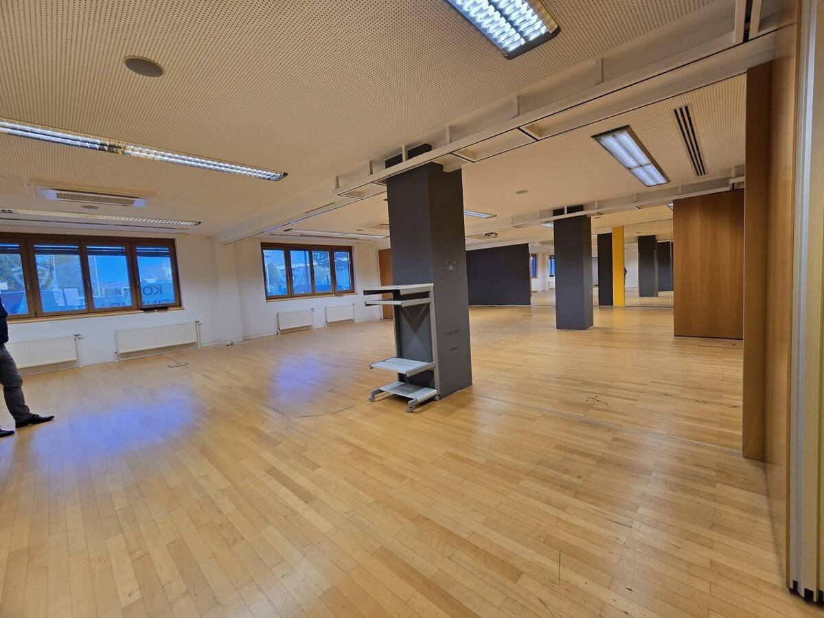 Geräumiger, offener Bürobereich mit Holzboden, Säulen und vielen Fenstern, ideal für Großraumbüros.