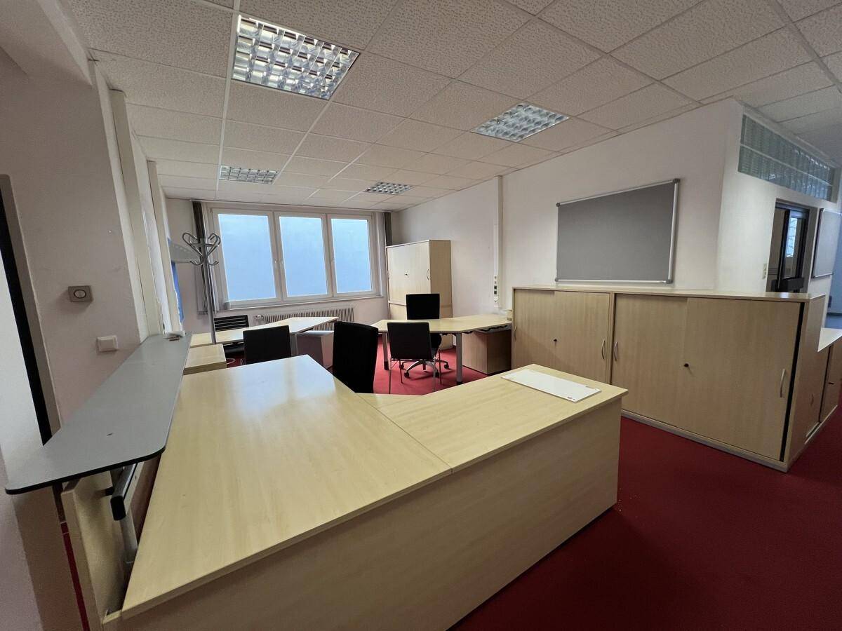 Geräumiges Büro mit mehreren Schreibtischen, Aktenschränken und rotem Teppichboden.