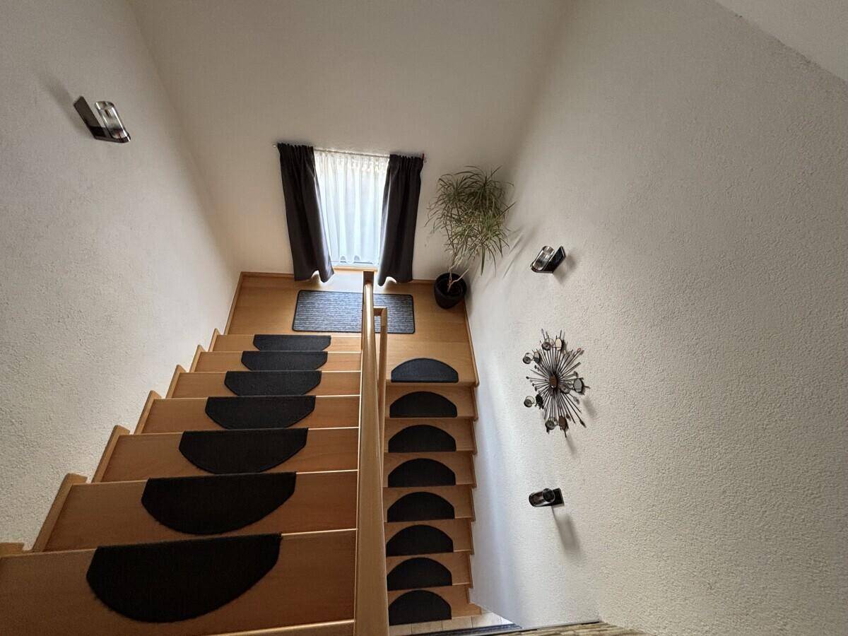 Holztreppe mit Teppichstufen und einem Fenster, das natürliches Licht hereinlässt.
