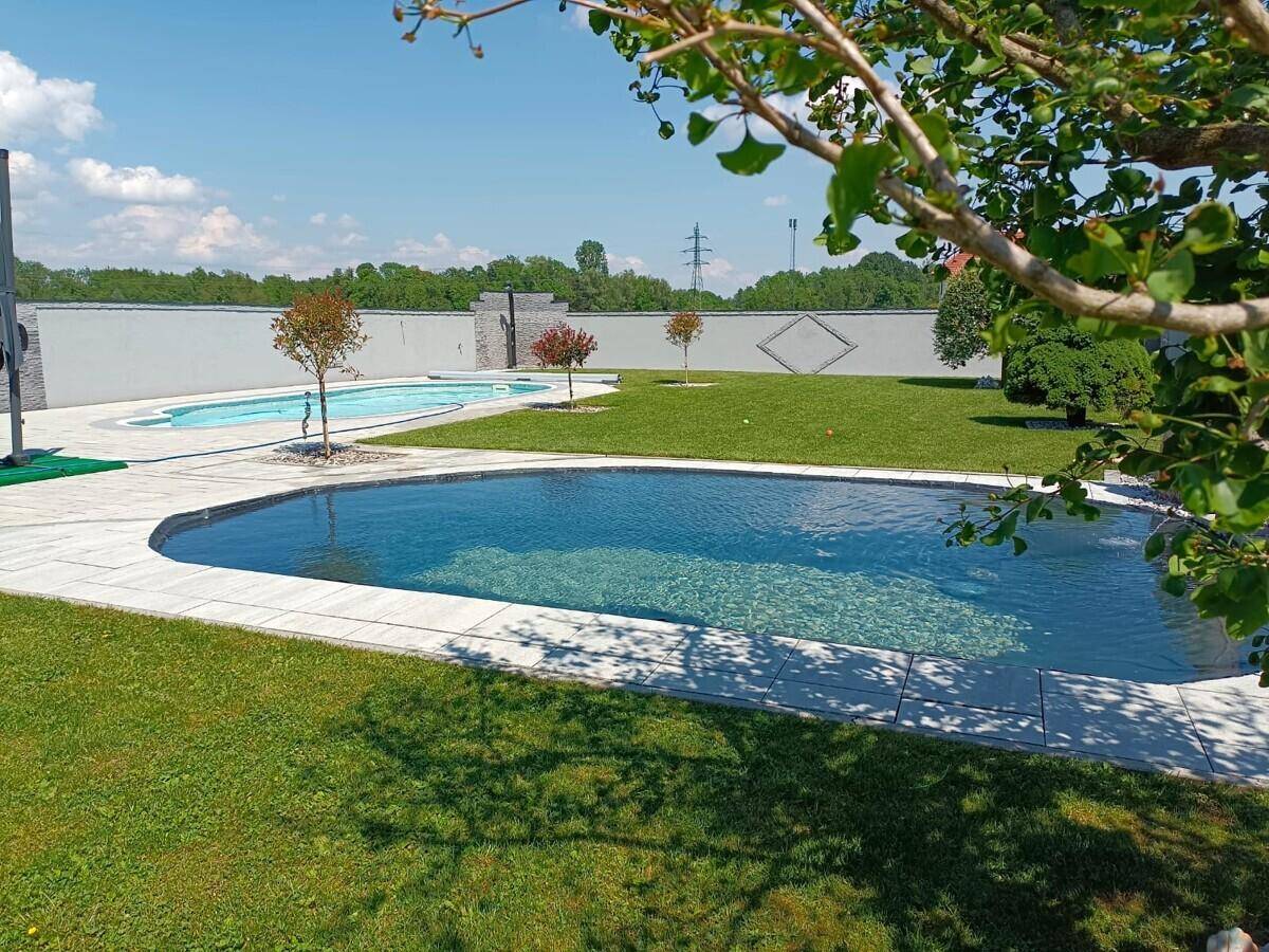 Zwei Pools in einer weitläufigen Gartenanlage mit gepflegtem Rasen und jungen Bäumen.