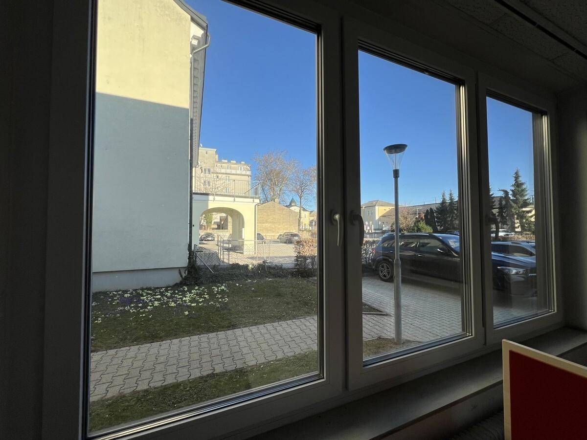 Blick aus einem Bürofenster auf den gepflasterten Außenbereich und die umliegenden Gebäude.
