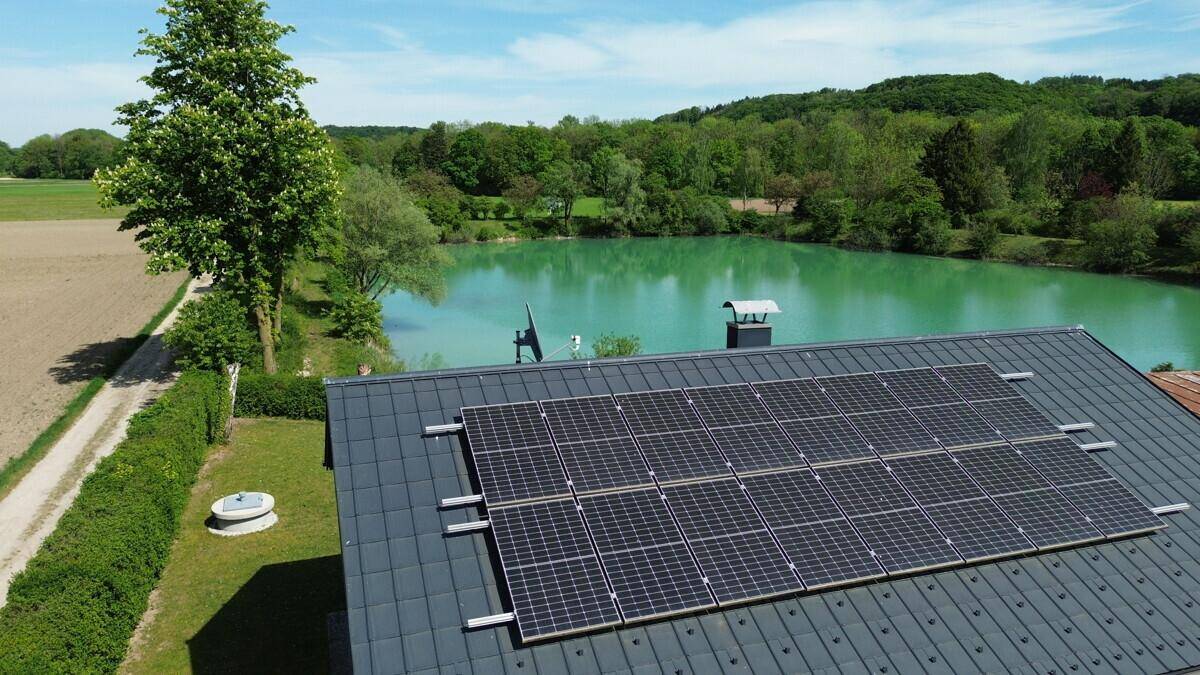 Nahaufnahme der Solaranlage auf dem Dach des Hauses mit türkisfarbenem See im Hintergrund.