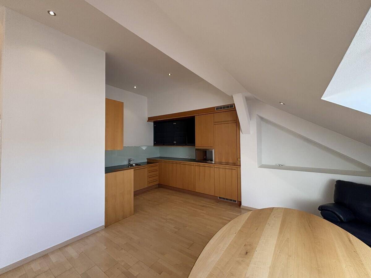 Moderne Küchenzeile im Dachgeschoss mit Holzschränken, integrierten Geräten und hellem Holzboden.