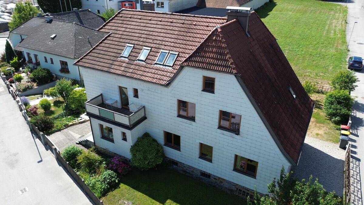 Ansicht des Hauses mit Balkon, gepflegtem Rasen und Blick auf die umliegende Natur.
