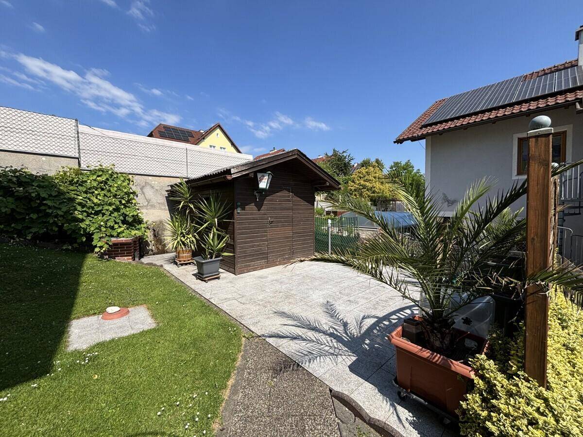 Gepflegter Gartenbereich mit Gartenhaus, Palmen und gepflastertem Weg.