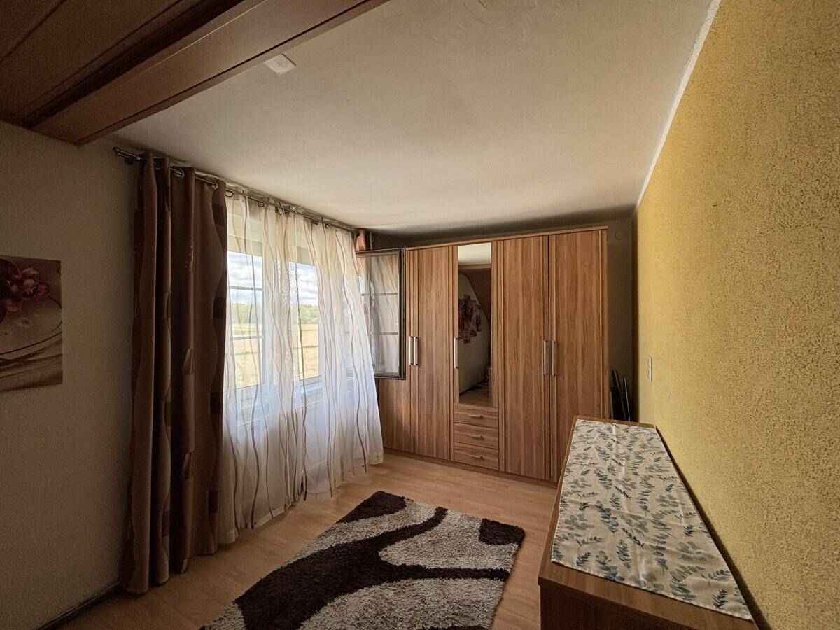 Schlafzimmer mit Holzboden, großem Kleiderschrank und gelber Akzentwand.