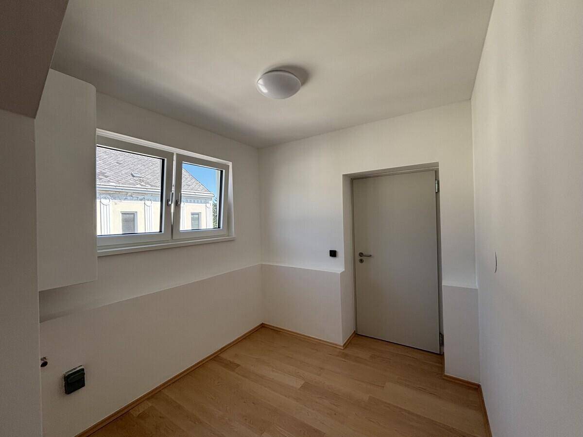 Heller Flur mit Fenster und Holzboden, der zu weiteren Räumen im Dachgeschoss führt.
