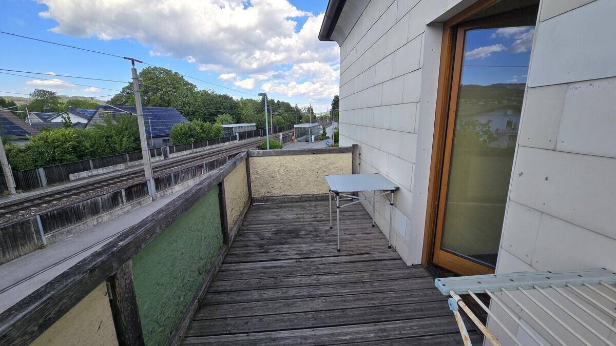 Kleiner Balkon mit Holzboden und einem Tisch, mit Blick auf Bahngleise und die Umgebung.