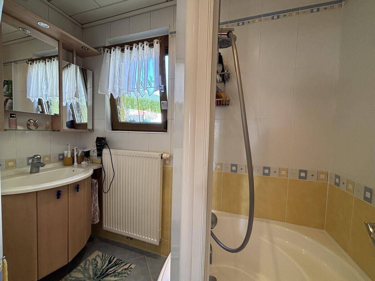 Helles Badezimmer mit Fenster, Waschbecken und Dusch-Badewannen-Kombination.