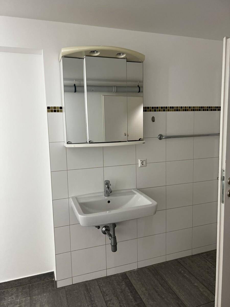 Badezimmer mit Waschbecken, Spiegelschrank und Handtuchhalter, gefliest in Weiß und Dunkel.