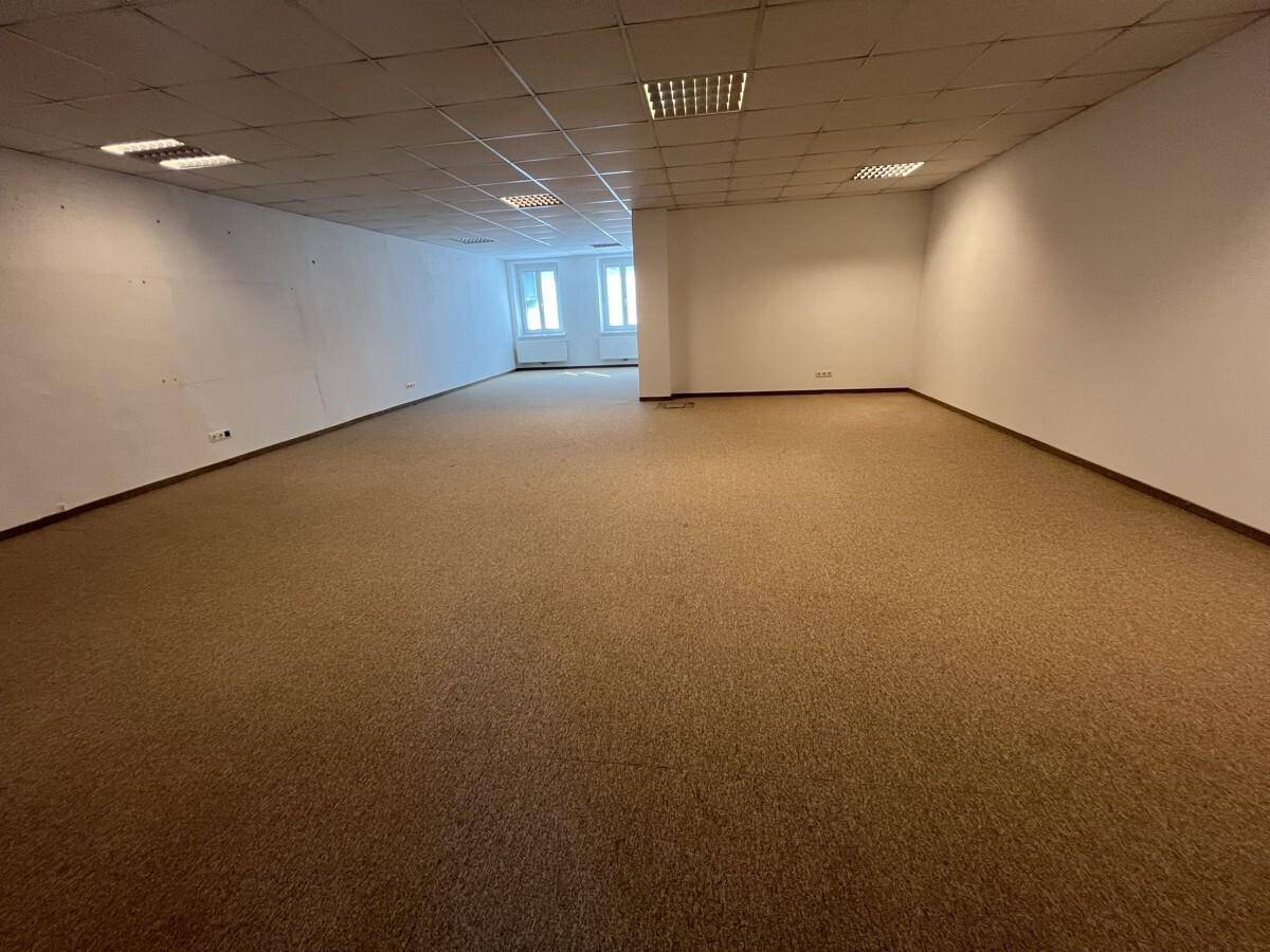 Weitläufiger, unmöblierter Bürobereich mit Teppichboden und Fenstern im Hintergrund, bereit zur Nutzung.