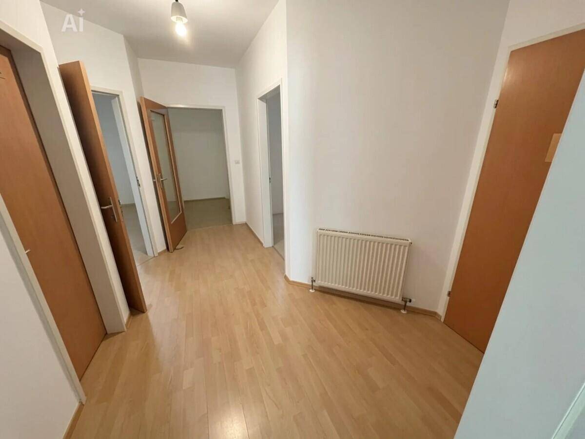 Heller Flur mit Laminatboden und weißen Wänden, verbindet mehrere Zimmer miteinander.