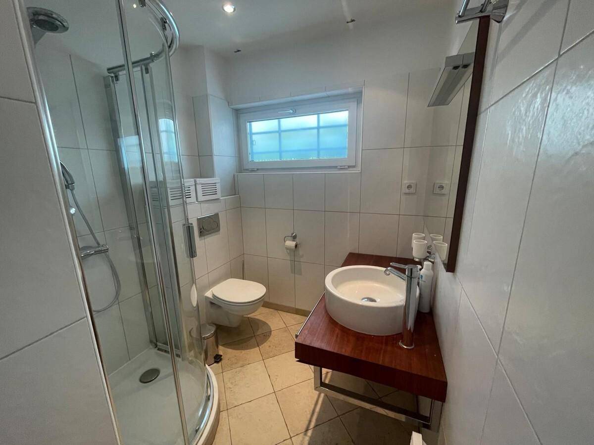 Modernes Badezimmer mit Duschkabine, wandhängendem WC und Fenster für Tageslicht.