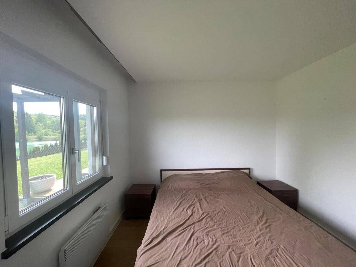 Schlafzimmer mit Doppelbett, Holzboden und großem Fenster mit Blick ins Grüne.