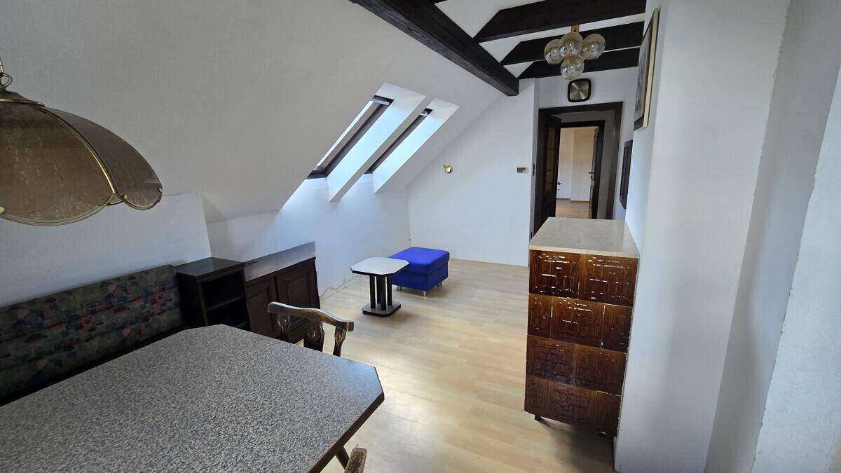 Gemütlicher Wohnbereich im Dachgeschoss mit sichtbaren Holzbalken, Dachfenstern und Kachelofen.