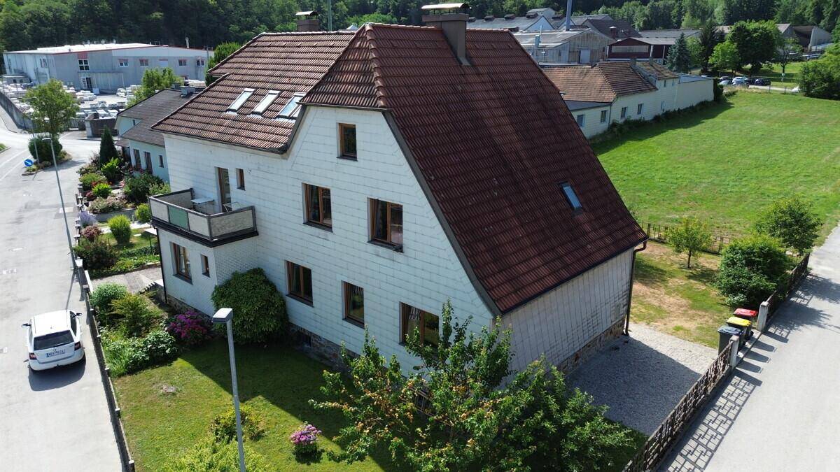 Ansicht des Hauses mit Balkon, Garten und angrenzendem Feld sowie Industriegebiet im Hintergrund.