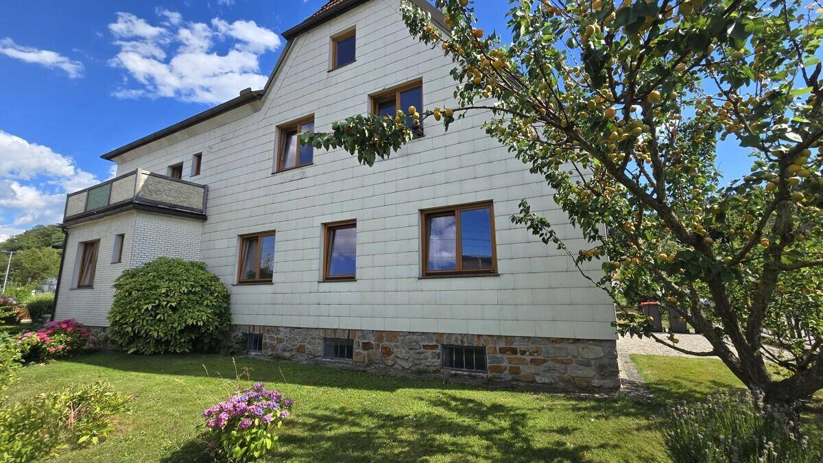 Seitenansicht des Hauses mit Balkon, gepflegtem Rasen und blühenden Sträuchern.