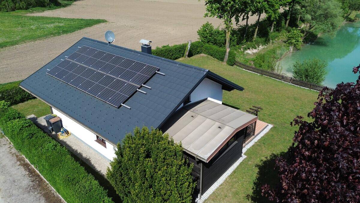 Luftaufnahme des Hauses mit Solarmodulen auf dem Dach und einem See im Hintergrund.