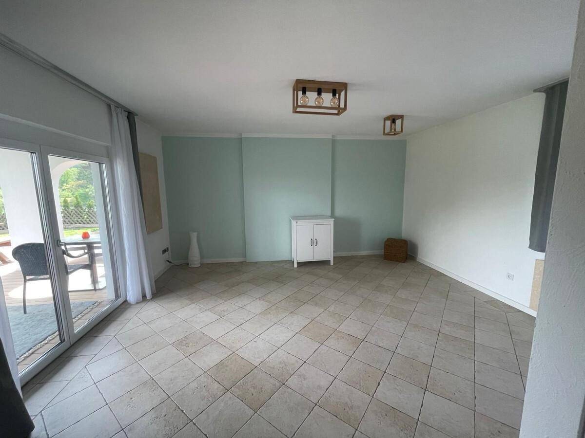 Geräumiges Wohnzimmer mit Fliesenboden, hellgrüner Akzentwand und Terrassenzugang.