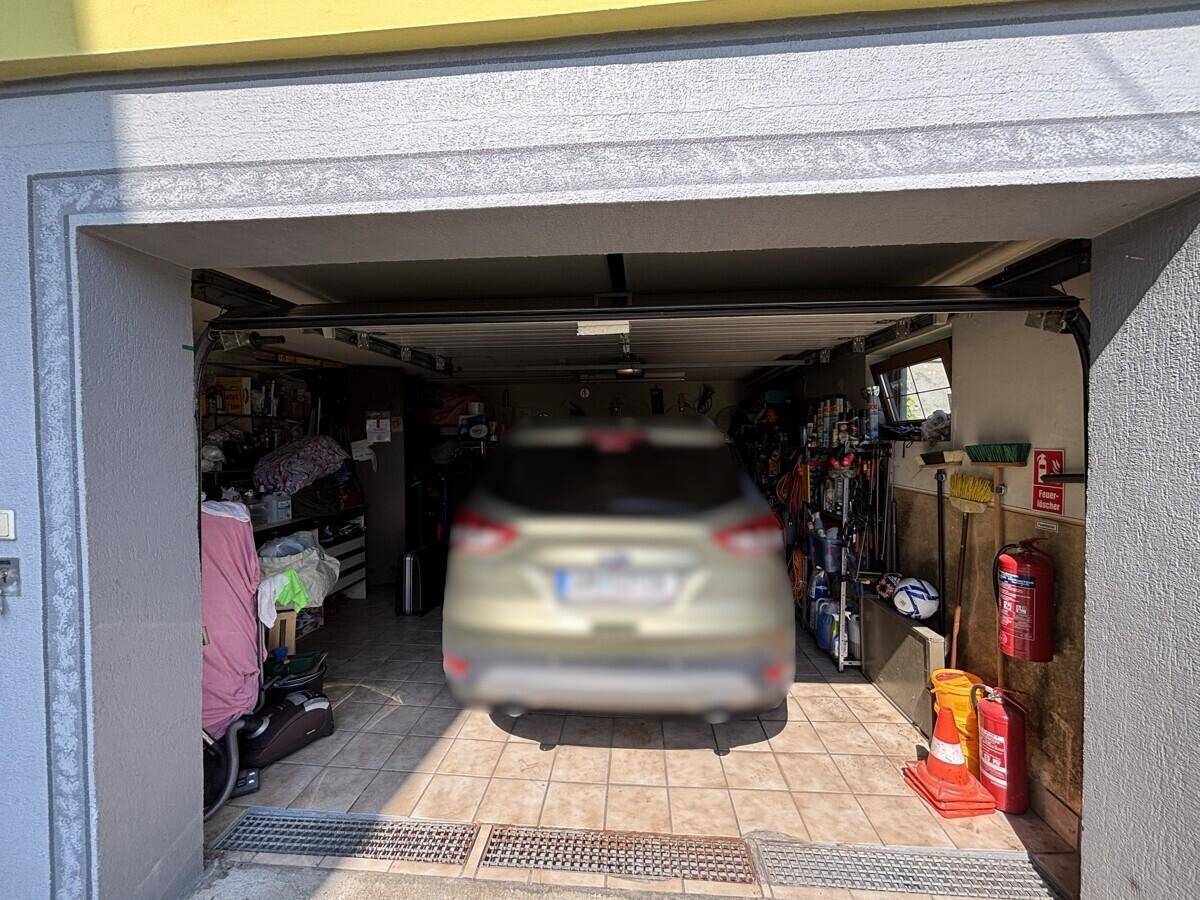 Geräumige Garage mit Fliesenboden, geparktem Auto und viel Stauraum.