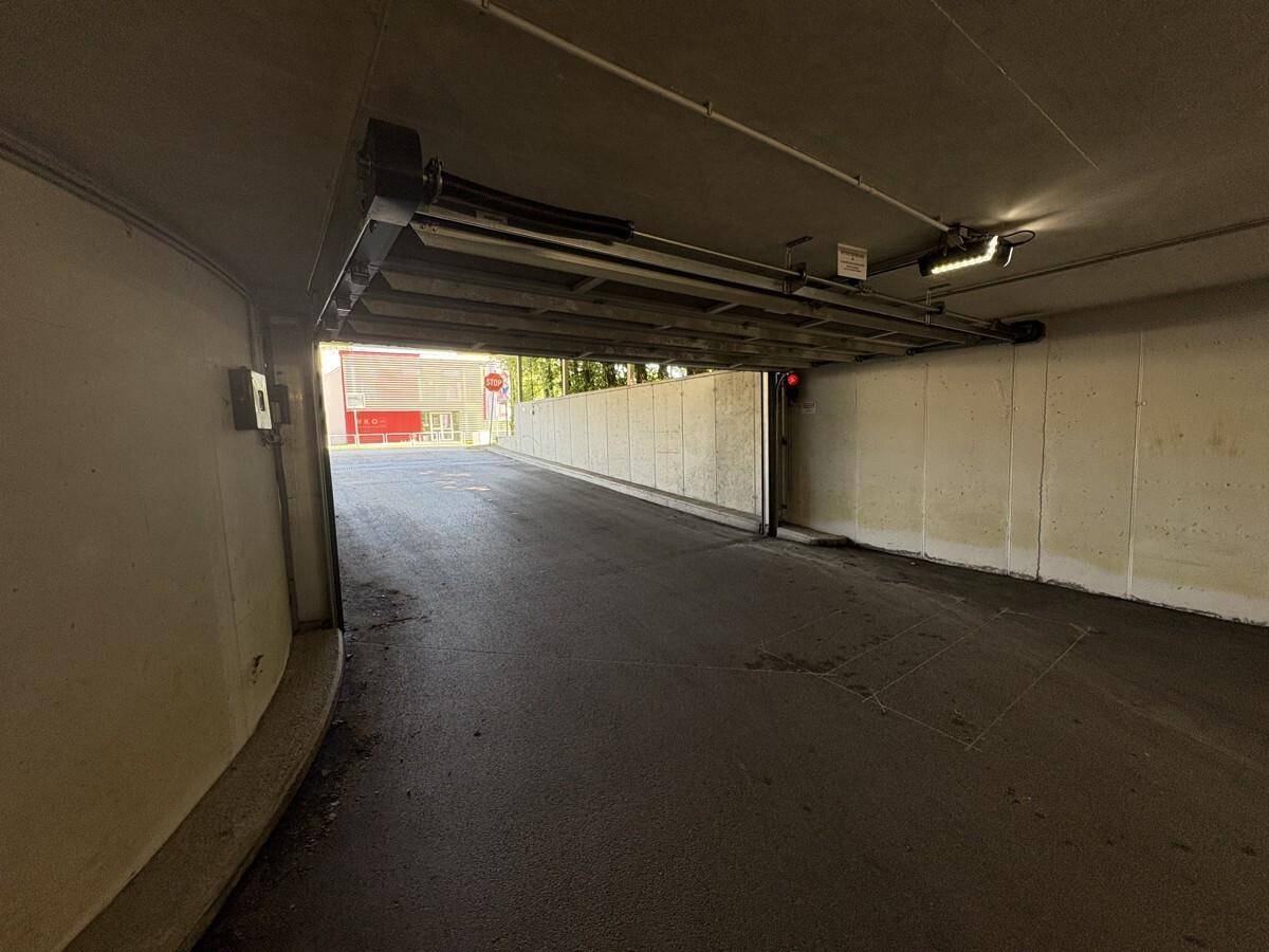 Einfahrt zur Tiefgarage mit automatischer Schranke und Betonwänden.
