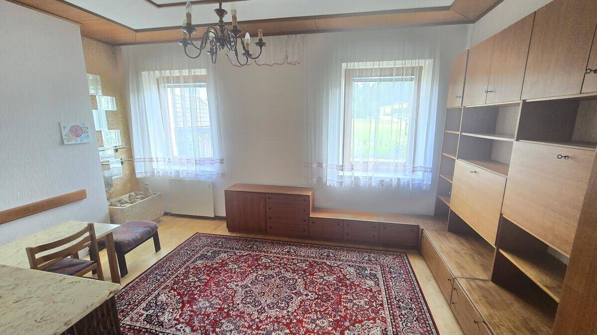 Wohnzimmer mit großem Teppich, Holzdecke und traditionellem Kronleuchter, hell und geräumig.