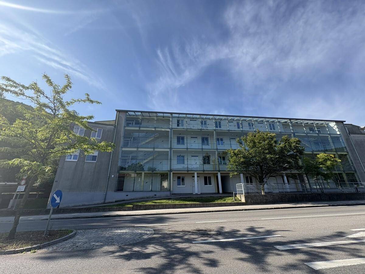 Moderne Gebäudefassade mit großen Glasflächen und Balkonen, direkt an einer Straße gelegen.