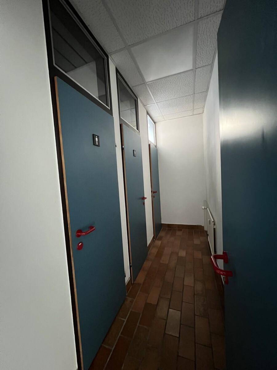 Flur mit mehreren Türen, wahrscheinlich zu Toiletten, und einem Terrakotta-Fliesenboden.