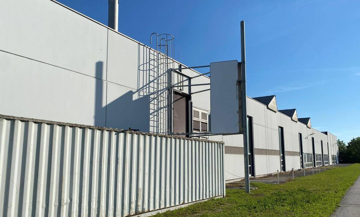 Seitenansicht eines Gewerbegebäudes mit Wartungsleiter und Lüftungselementen an der Fassade.