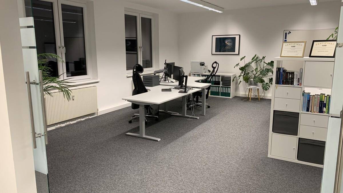 Geräumiges Büro mit zwei Arbeitsplätzen, großen Fenstern und einem Schiebetürsystem aus Glas.