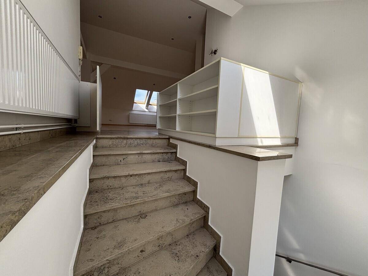 Steintreppe mit Geländer und integriertem Regal, die verschiedene Ebenen des Dachgeschosses verbindet.