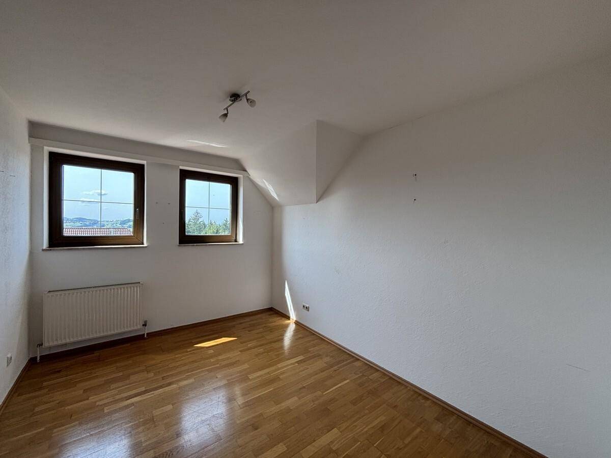 Schlafzimmer mit Holzparkett, zwei Fenstern und einer leichten Dachschräge.