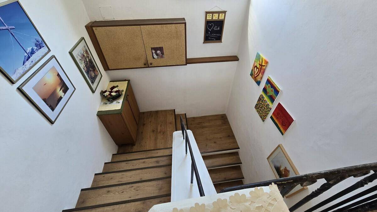 Treppenhaus mit Holzstufen, weiß gestrichenen Wänden und dekorativen Bildern.