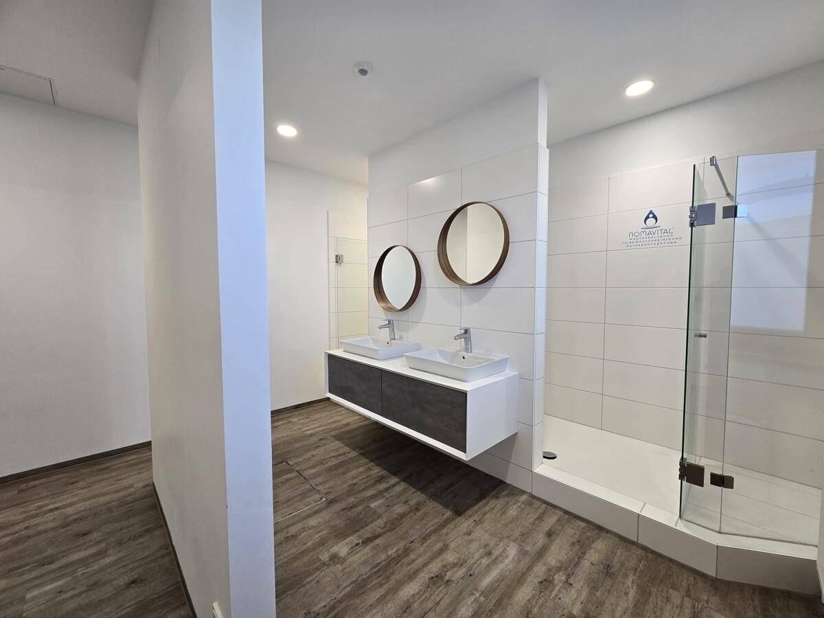 Modernes Badezimmer mit zwei Waschbecken, runden Spiegeln und einer begehbaren Dusche mit Glaswand.